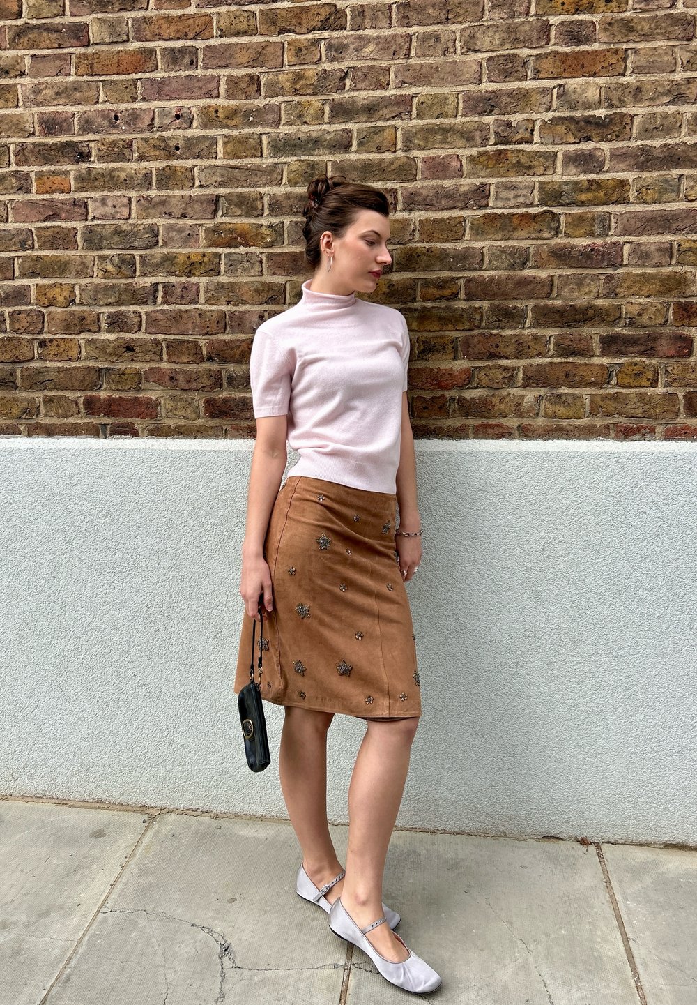 Lichtroze kortetermijn mock turtleneck, tan suedine kokerrok met bloemversieringen, grijze flats en een kleine zwarte handtas.