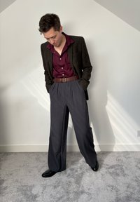 Pantaloni gri închis, cu croi larg, asortați cu o cămașă button-up burgundă și o curea maronie, completate cu un sacou texturat, de culoare închisă, și pantofi negri.