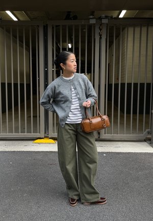 Cardigan gris tricoté sur une chemise rayée, pantalon large olive, et sac à main marron. Chaussures marron à bout rond. Couleur unie et design décontracté.