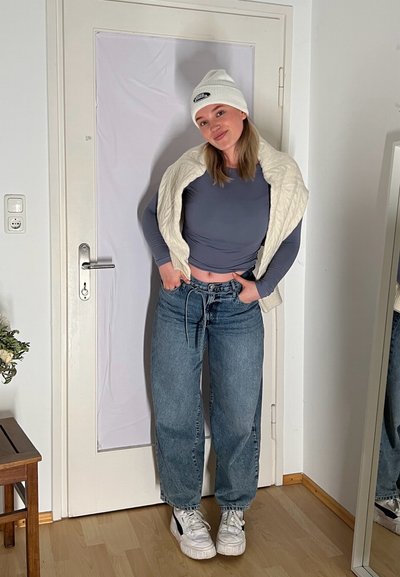 Conjunto casual que incluye una camiseta ajustada de manga larga gris, unos vaqueros de gran tamaño de color azul claro, un gorro de punto blanco y unas zapatillas blancas y gruesas.