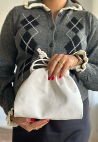 Fehér bőr kézitáska lekerekített formával és húzott felső résszel. Csomózott zsinórzáróval és sima textúrával rendelkezik.