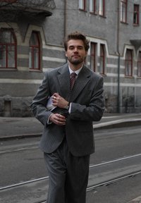 Grijs gestreept kostuum met jas en broek, wit hemd, rode gestreepte stropdas, een koffiekopje en een krant vasthoudend, staand op straat.