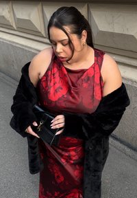 Piros virágos szatén maxiruha mély kivágással, fekete műszőrme kabáttal és egy kis fekete textúrált kézitáskával párosítva.