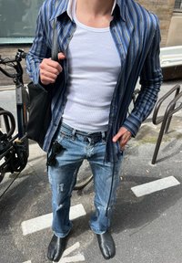 Stripete langermet skjorte i blått og hvitt, hvit tank top, slitte blå jeans og svarte ankelstøvler. Holder en svart totebag.