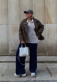 Καφέ δερμάτινο μπουφάν πάνω από ένα ριγέ πόλο, ναυτικές φόρμες, ασημένια τσάντα και παπούτσια με πλατφόρμα. Ένα γκρίζο καπέλο και γυαλιά ολοκληρώνουν την εμφάνιση.