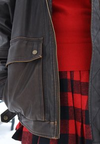 Veste en cuir noir partiellement dézippée sur un pull rouge côtelé et une jupe écossaise rouge et noire.