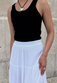 Μαύρο αμάνικο τοπ συνδυασμένο με λευκή φουστάνα με πιέτες. Η φουστάνα έχει μαλακή υφή, ενώ ένα ασημένιο κρεμαστό σε σχήμα καρδιάς κρέμεται σε μαύρο κορδόνι.