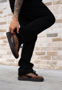 Brown and black trainers made from a combination of smooth and textured materials, featuring a low profile, lace-up design, and rubber sole.