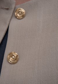 Tecido bege com uma superfície texturizada e dois botões circulares dourados com um design espiral no colarinho.