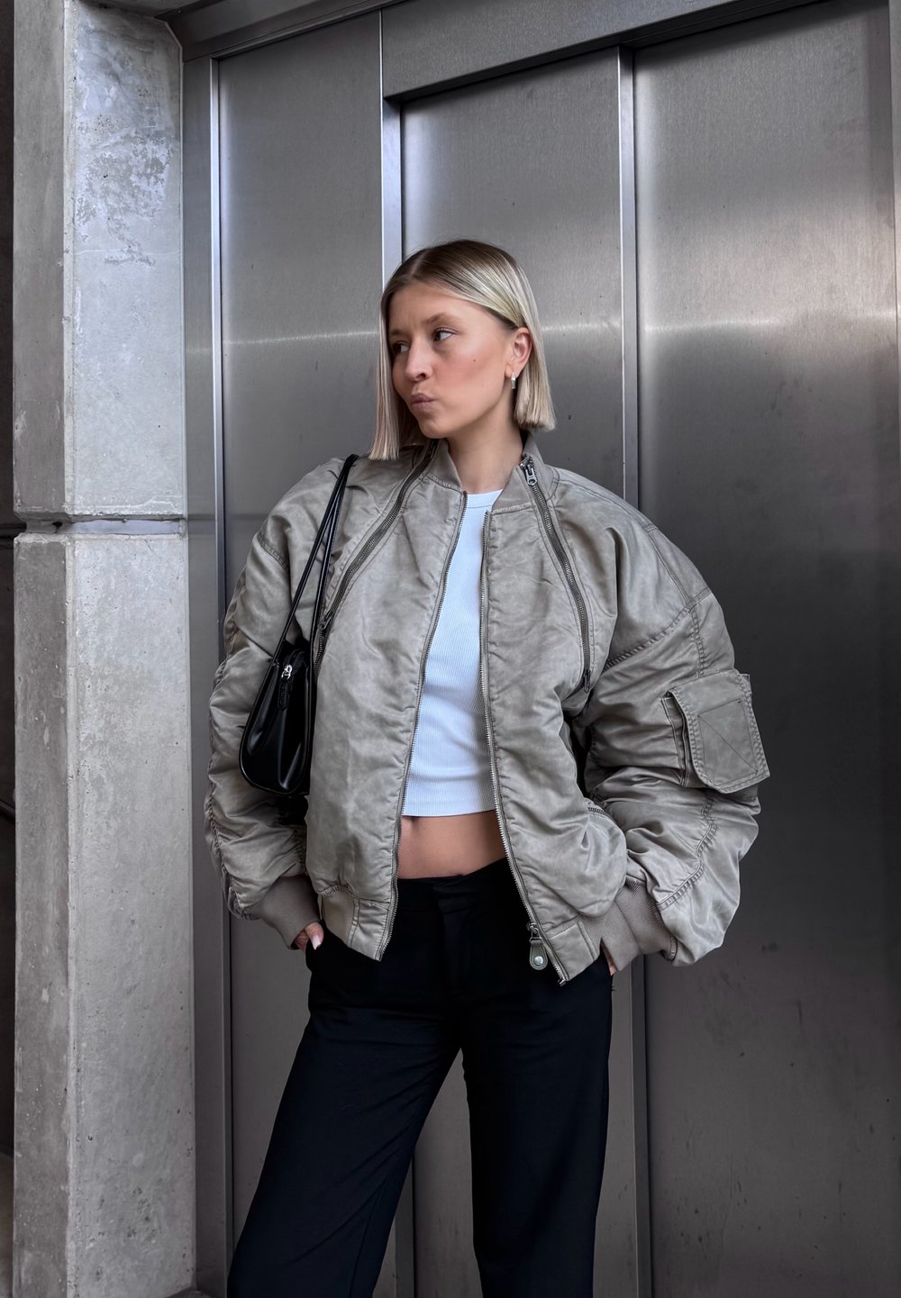 Gevoerde bomberjack in lichtgrijs, met een hoge kraag, geribbelde manchetten en zijzakken, gecombineerd met een cropped witte top en zwarte broek.