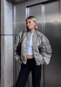 Gevoerde bomberjack in lichtgrijs, met een hoge kraag, geribbelde manchetten en zijzakken, gecombineerd met een cropped witte top en zwarte broek.