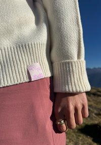 Krem pulover iz pletenine z rebrastimi manšetami, ki ima roza oznako. V kombinaciji z roza krilom. Ročno okrašen z dekorativnimi prstani.