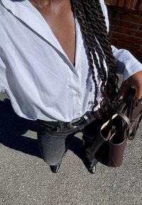 Camicia bianca con colletto, indossata sopra jeans scuri, abbinata a una borsa marrone. La camicia ha una vestibilità comoda e una texture liscia.