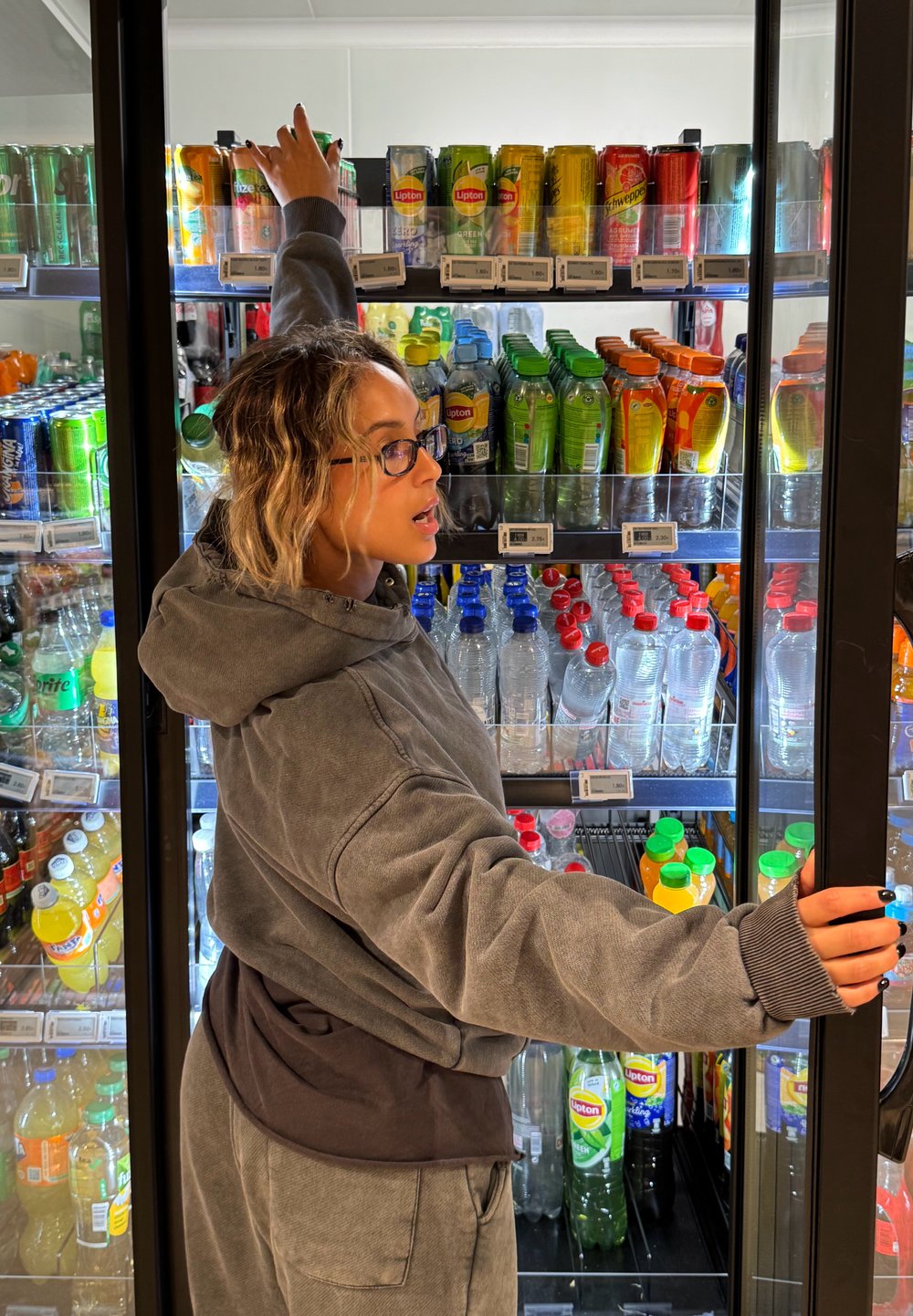 Espositore refrigerato per bevande con diverse lattine e bottiglie colorate. Articoli notevoli includono le bevande Lipton e bottiglie d'acqua in plastica trasparente.