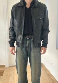Zwarte leren bomberjack met een voorkantsluiting, geribbelde manchetten en een borstzak, gedragen bij vervaagde blauwe spijkerbroek.