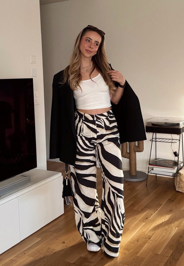 Schwarz-weiße, zebra-streifige weite Hosen, kombiniert mit einem kurzen weißen Oberteil und einem schwarzen Blazer. Die Accessoires umfassen eine kleine schwarze Handtasche.