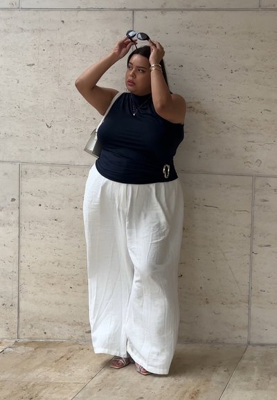 Top sin mangas azul marino con fruncidos, combinado con pantalones holgados de lino blancos. Los accesorios incluyen gafas de sol y un pequeño bolso de hombro.