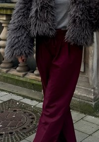 Φουντωτό γκρι ψεύτικο γούνινο εξωτερικό ρούχο με φαρδιές μανίκες, σε συνδυασμό με μπορντό παντελόνια φαρδιάς γραμμής, τονίζοντας την άνετη εφαρμογή και το χαλαρό στυλ.