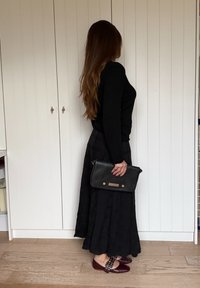 Must pikkade varrukatega topp, must kergelt volditud seelik, must käekott kuldsete detailidega ja burgundia-värvi kingad dekoratiivsete pandlatega.