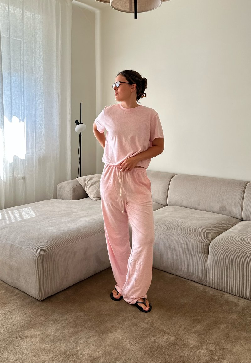 Conjunto de roupa de casa rosa claro, com uma parte de cima de manga curta e calças largas com cintura elástica. Textura suave, design casual.