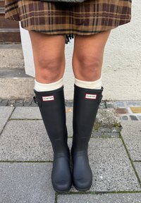 Bottes de pluie en caoutchouc noir avec logo, dotées d'un orteil arrondi, d'une texture lisse et d'un détail en boucle, accompagnées de chaussettes tricotées de couleur crème.