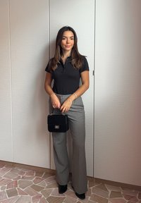 Czarny krótki rękaw polo, szare spodnie o wysokim stanie i szerokich nogawkach oraz mała czarna torebka z złotym zapięciem. Gładkie tekstury.