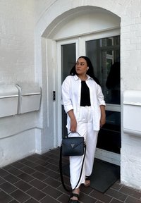 Hvit lin oversized skjorte over en svart topp, parret med hvite linbukser. Holder en svart håndveske med gullakkent; sandaler på føttene.