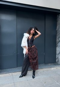 Musta vartaloa myötäilevä paita vetoketjulla, kerroksellinen ruskea hame pitsikoristein ja valkoinen turkistakki. Mustat korkokengät täydentävät asun.