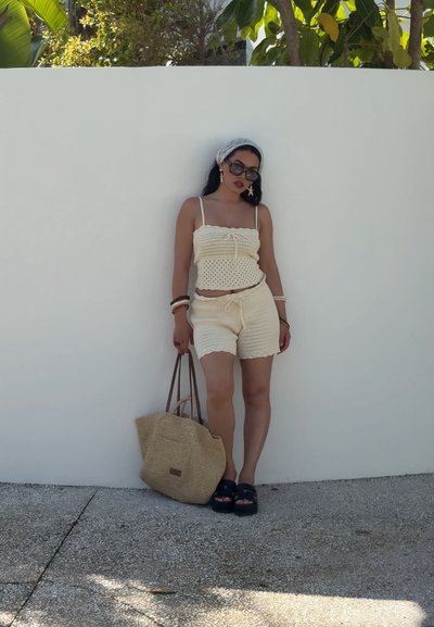 Conjunto de top y pantalones cortos de ganchillo en beige claro, con tirantes finos y cinturilla con cordón. Incluye bolsa de rafia tejida y calzado oscuro.