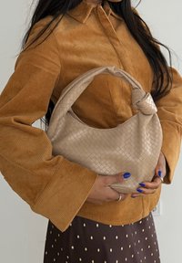 Personne portant une veste en velours côtelé moutarde et une jupe à pois, tenant un sac à main en cuir tressé beige avec une anse nouée.