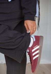 Zapatillas Adidas Spezial, de ante burdeos con rayas blancas, suela de goma y acentos azules. Combinan con pantalones negros holgados y calcetines blancos.