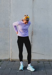 Purple long-sleeved athletic top with a half-zip, paired with black leggings. White socks and light blue running shoes complete the outfit.