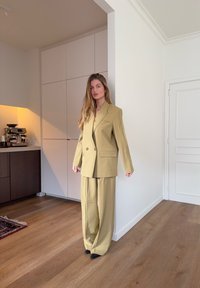 Costume vert pâle-brun, comprenant un blazer croisé et un pantalon à jambes larges, confectionné dans un tissu lisse avec des détails de couture minimes.
