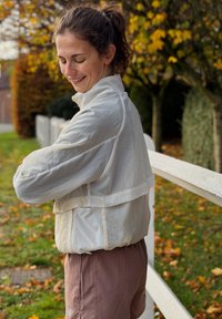 Lekka, biała, krótka kurtka z wysokim kołnierzem i szerokimi rękawami, zestawiona z luźnymi ró�żowymi szortami. Plener z jesiennymi liśćmi.