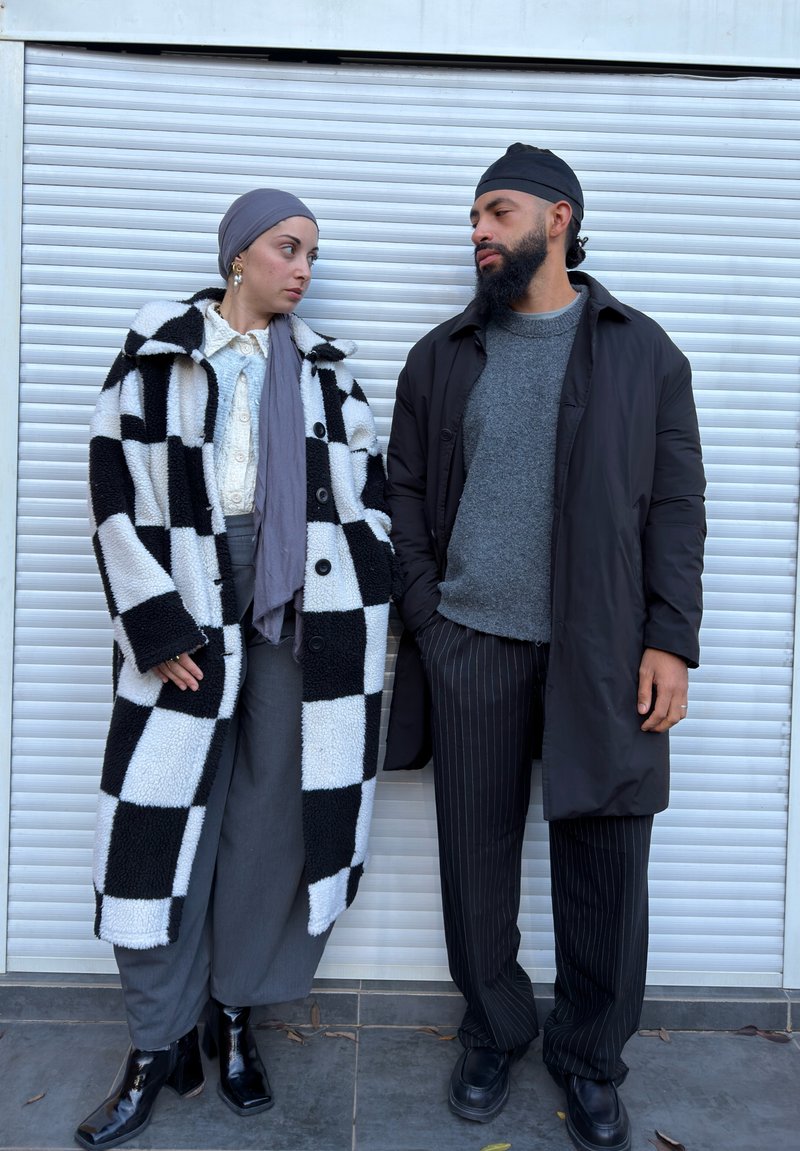 Manteau à damier noir et blanc, haut gris, écharpe grise et pantalon gris à jambes larges. Pantalon noir à fines rayures et bottes noires lisses.