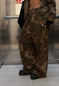 Brūnas kamuflāžas sporta bikses ar brīvu piegriezumu, elastīgu jostasvietu un sānu kabatām, apvienotas ar melnām platformas kurpēm.