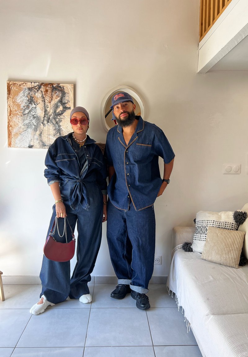 Outfit in jeans blu scuro; uno ha una camicia legata sopra pantaloni larghi, l'altro una camicia a maniche corte con pantaloni abbinati. Gli accessori includono una borsa bordeaux.