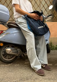 Høje lyseblå jeans, brune sko med hvide striber, hvid t-shirt og en blå tote bag, der hviler på en lyseblå scooter.