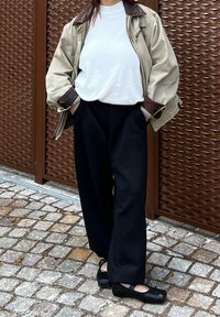 Beige oversize bunda s tmavě hnědým límcem, bílý žebrovaný top, černé široké kalhoty a černé boty s mašlí. Pozadí z kostek.