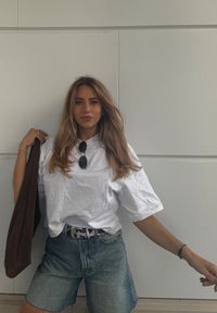 Λευκό φαρδύ T-shirt, ανοιχτό μπλε τζιν σορτς, ζώνη με σχέδιο, καφέ τσάντα. Χαλαρά μαλλιά και γυαλιά ηλίου ολοκληρώνουν το αθλητικό στυλ.