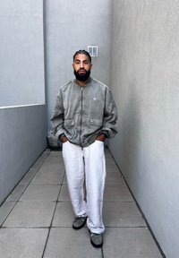 Gray bomber jacket with a zip front, oversized fit, and two front pockets. White linen pants and gray sneakers. Smooth texture, relaxed design.