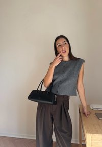 Szary skrócony sweter na guziki z przodu, zestawiony z luźnymi brązowymi spodniami i czarną skórzaną torebką z dwoma uchwytami i zamkiem błyskawicznym.