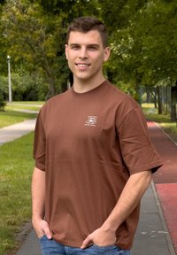 Marron t-shirt de coton à manches courtes et col rond, avec un petit détail graphique blanc sur la poitrine. Porté avec un jean bleu.