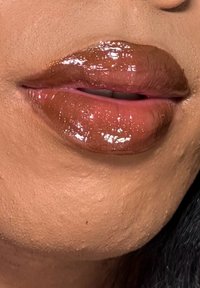 Glansful brun leppestift på fyldige lepper, som fremhever en jevn tekstur med subtil glans. Hudtonen ser jevn og naturlig ut.