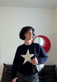 Pull bleu marine avec un grand motif étoile crème sur le devant, fabriqué en tissu tricoté texturé ; assorti à un sac à épaule noir.