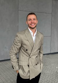 Svijetlosivi dvostruki sako s vertikalnim prugama, crnim dugmadima i teksturiranom tkaninom, nosi se preko bijele košulje, uz crne hlače.