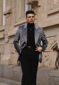 Szary aksamitny żakiet z wywijanymi klapami, czarny golf, czarny pasek i spodnie. Prosta srebrna naszyjnik podkreśla całość.