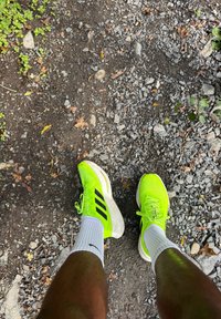 Lyse neongrønne sportsko med svarte striper, kombinert med hvite ankelsokker, plassert på en grusvei.
