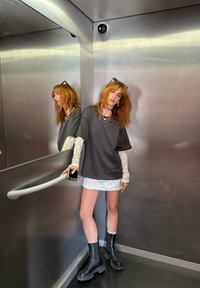 Crna oversized majica, mini suknja s srebrnim šljokicama, čipkaste rukave i crne čizme na debelu petu u ogledalu liftu s metalnim zidovima.