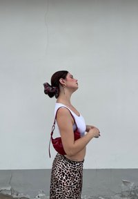 Weißes Crop-Top, Rock mit Leopardenmuster und rote Ledertasche. Haare mit einem schwarz-roten Scrunchie zusammengebunden. Goldene Creolen.